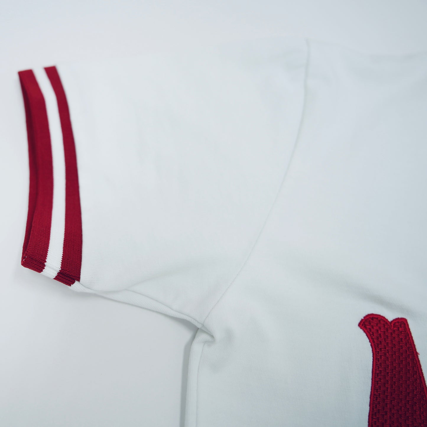 White sports outfit with red accents on a light gray background.The Kappa Alpha Psi "Nupe" T-shirt is a collectible item that represents the historical significance and traditions of the fraternity . It serves as a symbol of pride and belonging for members and supporters of Kappa Alpha Psi. This t-shirt is a unique piece of memorabilia that showcases the unique cultural heritage and shared values of those involved in the organization.