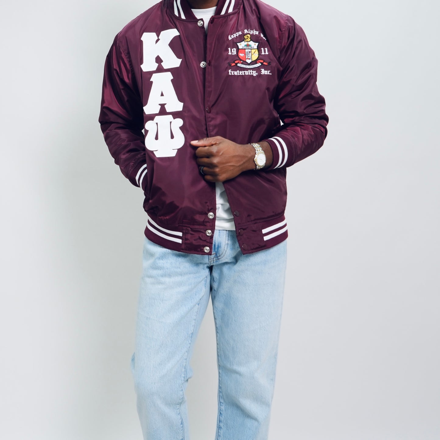 Person wearing a maroon letterman jacket with 'Kappa Alpha Psi' letters on a plain background.Check out our Kappa Alpha Psi satin jacket selection for the very best in unique design. This Kappa Alpha Psi Baseball Nylon Jacket shows the fraternity Shield embroidered on left chest and Greek letters on right to create style and unique comfort in wear. Quality beyond imagination.