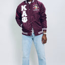 Person wearing a maroon letterman jacket with 'Kappa Alpha Psi' letters on a plain background.Check out our Kappa Alpha Psi satin jacket selection for the very best in unique design. This Kappa Alpha Psi Baseball Nylon Jacket shows the fraternity Shield embroidered on left chest and Greek letters on right to create style and unique comfort in wear. Quality beyond imagination.
