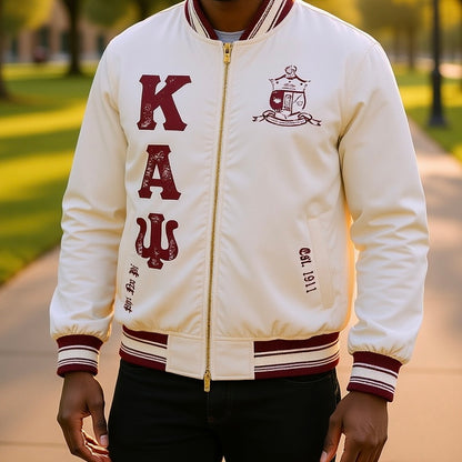 cream jacket with red lettering and emblem, worn outdoors on a blurred background.The Kappa Alpha Psi Cream Twill Jacket is a stylish and classic outerwear option for men. Made with durable twill material, this jacket features the signature ivory/ cream color of the Nupe Kave brand. It is designed with regular sizing in mind, making it a versatile option for a variety of men's sizes. Perfect for adding a touch of sophistication to any outfit, this jacket is a must-have for any man looking to showcase.