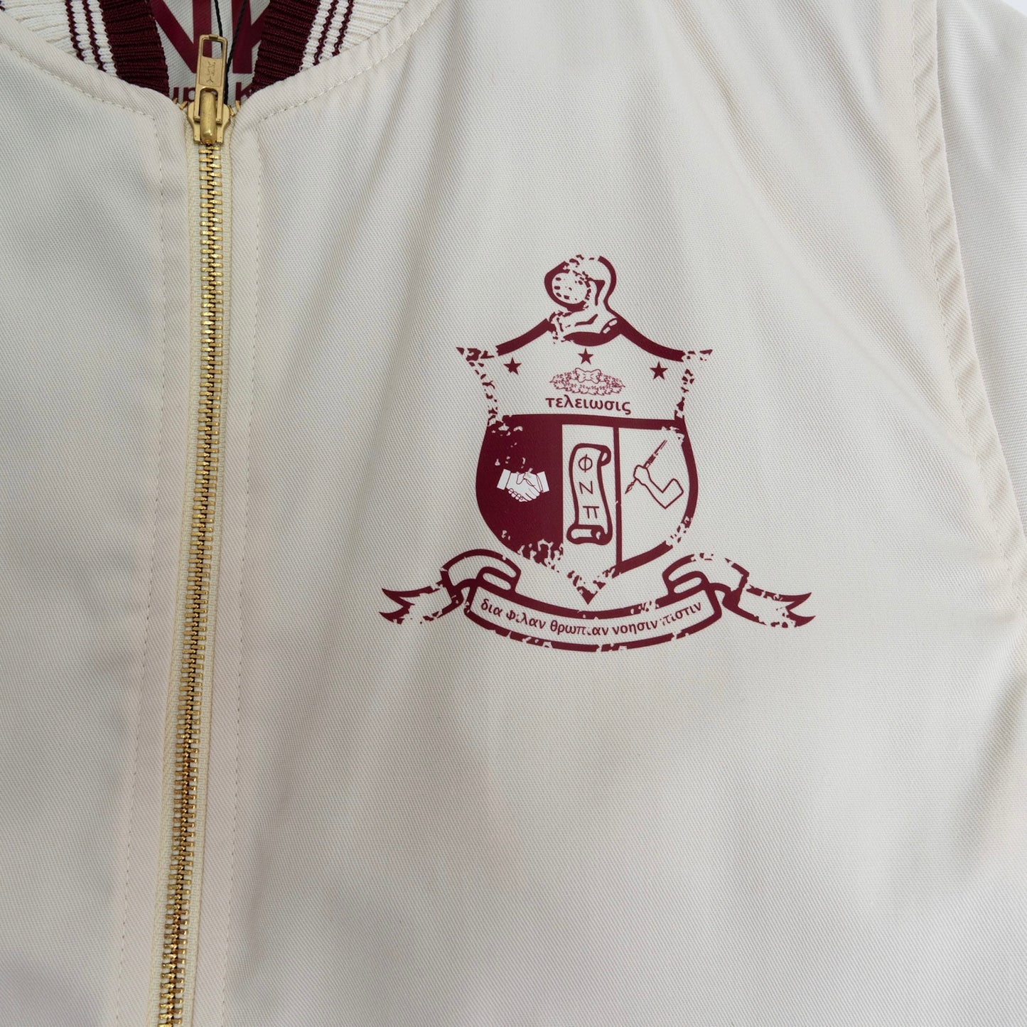 White jacket with a gold zipper and maroon crest design on the chest.The Kappa Alpha Psi Cream Twill Jacket is a stylish and classic outerwear option for men. Made with durable twill material, this jacket features the signature ivory/ cream color of the Nupe Kave brand. It is designed with regular sizing in mind, making it a versatile option for a variety of men's sizes. Perfect for adding a touch of sophistication to any outfit, this jacket is a must-have for any man looking to showcase.