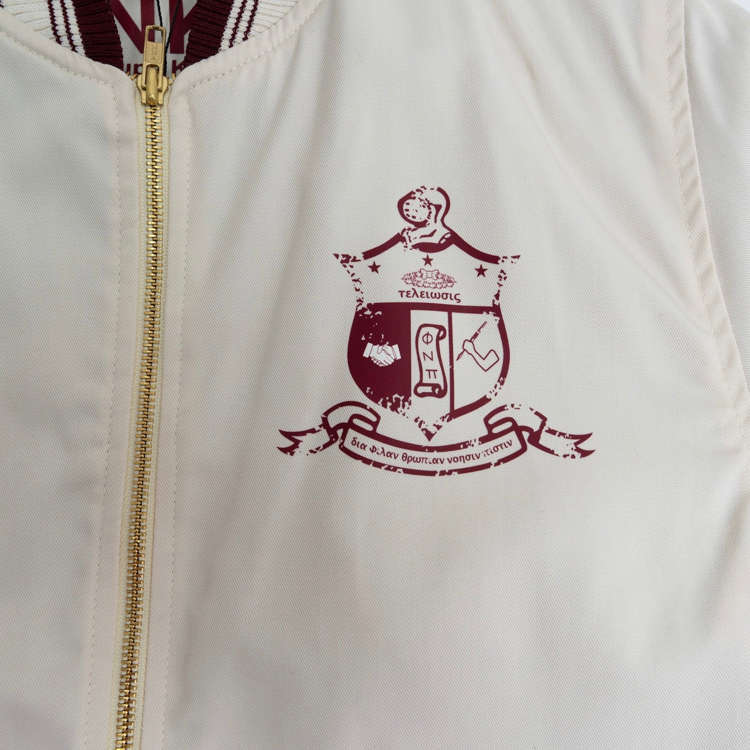 White jacket with a gold zipper and maroon crest design on the chest.The Kappa Alpha Psi Cream Twill Jacket is a stylish and classic outerwear option for men. Made with durable twill material, this jacket features the signature ivory/ cream color of the Nupe Kave brand. It is designed with regular sizing in mind, making it a versatile option for a variety of men's sizes. Perfect for adding a touch of sophistication to any outfit, this jacket is a must-have for any man looking to showcase.