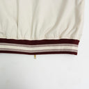 Close-up of a beige jacket with a brown and white striped hem on a white background.The Kappa Alpha Psi Cream Twill Jacket is a stylish and classic outerwear option for men. Made with durable twill material, this jacket features the signature ivory/ cream color of the Nupe Kave brand. It is designed with regular sizing in mind, making it a versatile option for a variety of men's sizes. Perfect for adding a touch of sophistication to any outfit, this jacket is a must-have for any man looking to showcase.