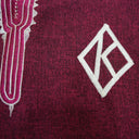 Close-up of a maroon fabric with white embroidered design.The product is Kappa Alpha Psi African Wear, specifically designed for members of the prestigious African American fraternity. This apparel is a symbol of pride and unity among the members of the organization, showcasing their heritage and cultural background. With the iconic symbols and colors of Kappa Alpha Psi, this African wear is a must-have for any member looking to represent their fraternity in a stylish and meaningful way.
