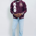 Person wearing a maroon letterman jacket with white text and light blue jeans on a plain background.Check out our Kappa Alpha Psi satin jacket selection for the very best in unique design. This Kappa Alpha Psi Baseball Nylon Jacket shows the fraternity Shield embroidered on left chest and Greek letters on right to create style and unique comfort in wear. Quality beyond imagination.
