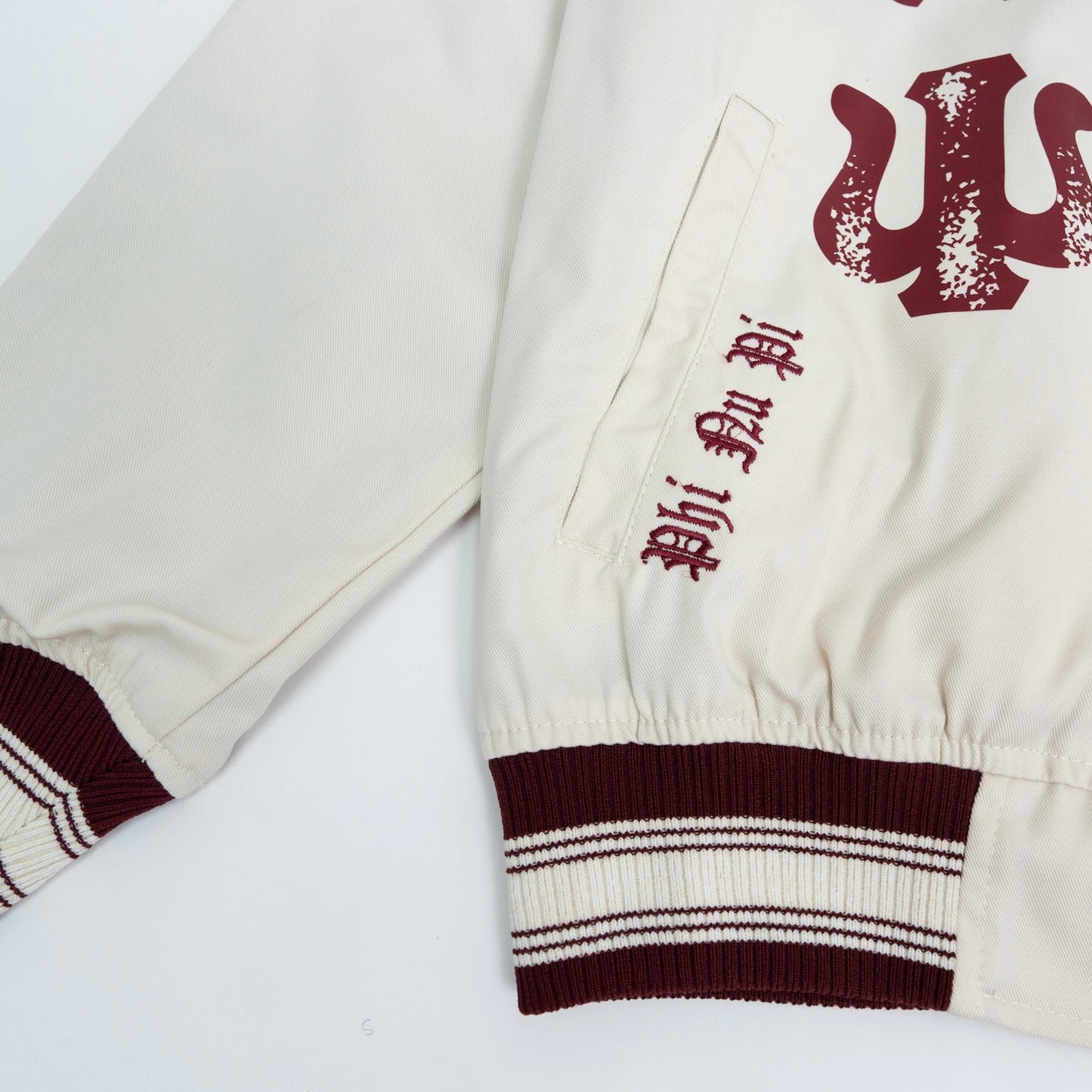 Close-up of a cream-colored varsity jacket with red lettering on a white background.The Kappa Alpha Psi Cream Twill Jacket is a stylish and classic outerwear option for men. Made with durable twill material, this jacket features the signature ivory/ cream color of the Nupe Kave brand. It is designed with regular sizing in mind, making it a versatile option for a variety of men's sizes. Perfect for adding a touch of sophistication to any outfit, this jacket is a must-have for any man looking to showcase.