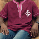 Person wearing a maroon shirt with white embroidery sitting on a brown. couch.The product is Kappa Alpha Psi African Wear, specifically designed for members of the prestigious African American fraternity. This apparel is a symbol of pride and unity among the members of the organization, showcasing their heritage and cultural background. With the iconic symbols and colors of Kappa Alpha Psi, this African wear is a must-have for any member looking to represent their fraternity in a stylish and meaningful way.